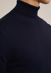 Jūras spēku turtlenecks džemperis, pieguļošs dizains. Izgatavots no mīksta adījuma auduma, ar augstu apkakli un ribotu tekstūru ap kaklu.