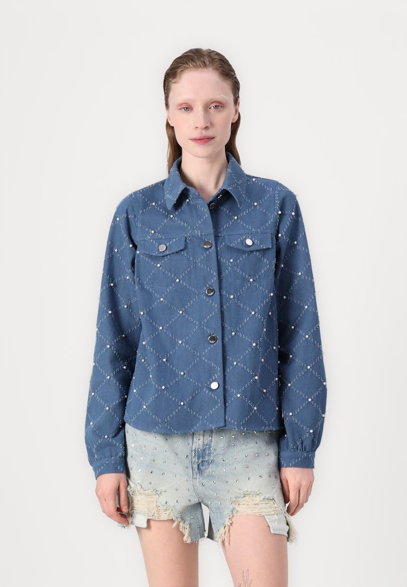 Blå denimjakke med diamantmønster og sølvnitter, to brystlommer og knapping foran. Lange ermer og avslappet passform.