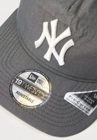 Γκρι καπέλο από ύφασμα με καμπυλωτό γείσο. Διαθέτει λευκό κεντημένο λογότυπο "NY", ρυθμιζόμενο λουρί και πολλές ετικέτες της μάρκας στο γείσο.