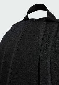Zaino in tessuto nero con superficie testurizzata, dotato di manico superiore e cuciture strutturate, che enfatizzano un design semplice e pratico.