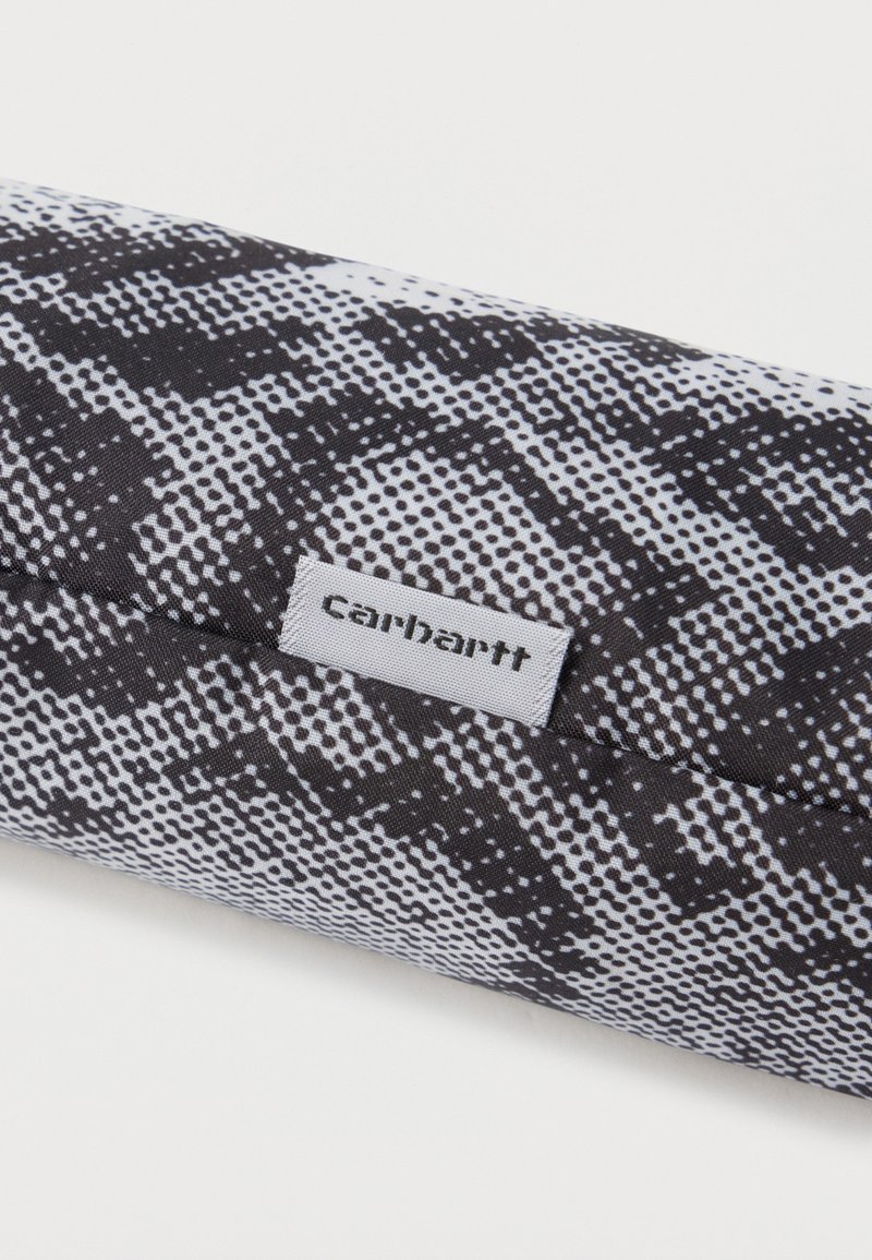 Tissu imprimé serpent en noir et blanc avec une étiquette de marque Carhartt blanche cousue sur un article textile plié.