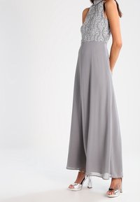 Gray halter gown with a patterned bodice, flowing skirt, and sheer fabric. Silver heeled sandals complete the outfit.