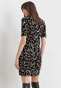 Schwarzes, knielanges Kleid mit kurzen Ärmeln und einem beigen abstrakten Muster. Der Stoff hat eine strukturierte Oberfläche.