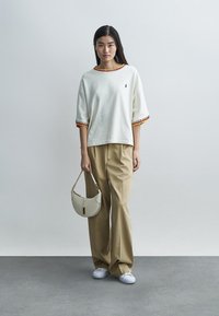 Pulover alb cu mâneci scurte și dungi, cu margini roșii și galbene, asortat cu pantaloni bej cu picioare largi și o geantă de mână gri deschis. Adidași albi.