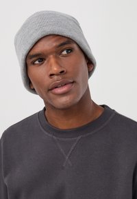 Szary prążkowany beanie noszony przez osobę, o dopasowanym fasonie. Osoba jest w ciemnoszarej bluzie, lekko zwrócona w górę.