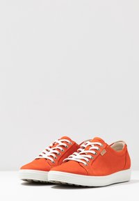 Zapatillas casuales de color naranja brillante con cordones y suelas blancas, diseño de corte bajo y una pequeña etiqueta de la marca en el lateral, sobre un fondo plano.