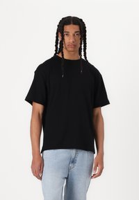 Tricou scurt negru din bumbac, cu un croi lejer, asociat cu blugi din denim de un albastru deschis. Design simplu, fără embellishments vizibile.