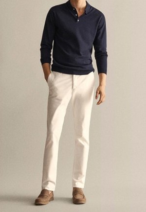 Granatowa dzianinowa koszulka henley, białe spodnie, brązowe buty. Koszulka ma trzy guziki w dekolcie; spodnie są proste z kieszeniami.