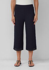 Marineblauwe culottes van een gestructureerde stof met een golvend patroon en een geschulpte zoom, gecombineerd met zwarte platte sandalen.