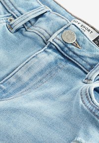 Jasnoniebieskie szorty dżinsowe zbliżenie na pas, guzik oznaczony "Next Denim", szlufki na pasek oraz metka z napisem "Boy Short".