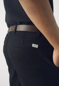 Črne bombažne hlače z gladko teksturo, ki vključujejo rjav pas in zadnji žep s priponkami Jack & Jones.
