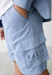 Ljusblå shorts i mjukt material med en sidficka och tryckt märkesnamn "BAKER by Ted Baker" på den nedre sidan.
