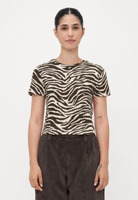 T-shirt a strisce zebrate marrone e crema con scollo tondo e maniche corte, abbinato a pantaloni in velluto a coste marroni con chiusura a bottone.