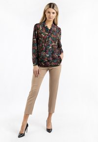 Blusa con stampa floreale in tonalità scure, con maniche lunghe, abbinata a pantaloni beige aderenti e tacchi alti neri. Tessuto liscio con una leggera lucentezza.