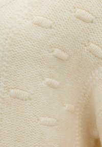 Tissu tricoté de couleur crème avec des points en relief horizontaux créant une surface texturée subtile.