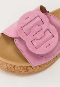 Sandalo in suede rosa con una grande fibbia circolare, suola in sughero e finitura testurizzata. Il design presenta una cintura ampia e una fodera morbida.