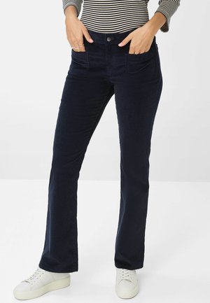 Navy Baumwollcordhose im Slim-Fit, mit Fronttaschen und Knopfverschluss, kombiniert mit weißen Sneakern.