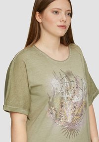Oliwkowa koszulka z krótkim rękawem o okrągłym dekolcie, z kwiatowym wzorem w delikatnych kolorach i podwiniętymi mankietami.
