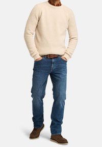Maglione crema in maglia a coste con scollo tondo, abbinato a jeans di denim blu. Scarpe in pelle marrone completano l'outfit.