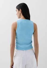 Lichtblauw geribbeld mouwloos topje met een aansluitend ontwerp en een gestructureerde afwerking, gecombineerd met witte hoge taille broek met ruching aan de achterkant.