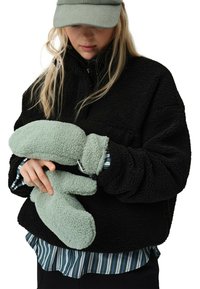 Czarna polarowa kurtka z wysokim kołnierzem, noszona na paskowanym T-shircie. Model trzyma miękki, miętowy pluszowy przedmiot przypominający rękawiczki.