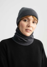 Grau gerippte Strickmütze und passender Loop, beide aus strukturiertem Material gefertigt. Kombiniert mit einem schwarzen Pullover für einen stimmigen Look.