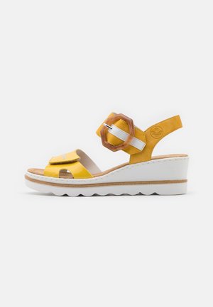 Sandales compensées jaunes avec une bride brillante présentant une découpe, une boucle blanche et une semelle intérieure en cuir brun texturée. Semelle plateforme blanche.