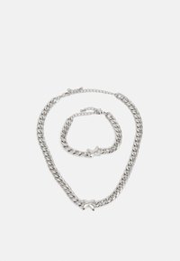 Ensemble collier et bracelet en chaîne argentée, présentant un design à maillons épais avec un accent étoile. Texture lisse, finition polie, longueurs ajustables.