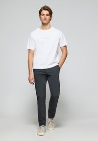 Biała koszulka z krótkim rękawem z napisem "Polo Club", zestawiona z ciemnoszarymi spodniami slim-fit i beżowymi trampkami. Prosty, czysty design.