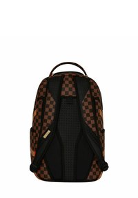 Mochila de cuadros marrón y negro con correas acolchadas y texturizadas y bolsillos laterales. Presenta un asa en la parte superior y detalles de marca.