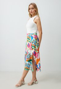 Witte mouwloze top gecombineerd met een kleurrijke midi-rok met bloemenprint en een zijsplit. De rok heeft levendige patronen in roze, blauw en oranje.