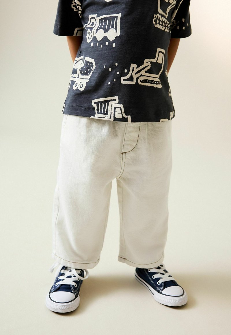 White denim wide-leg pants paired with a black t-shirt featuring white construction vehicle patterns. Dark blue sneakers with white laces.