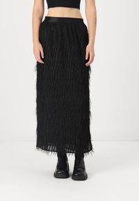 Black mid-length skirt with textured fringe fabric and a smooth waistband, paired with black chunky shoes. The overall design is simple and modern.
