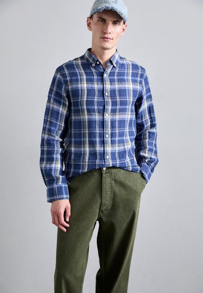 Μπλέ και λευκό καρό πουκάμισο με μακριά μανίκια, σε συνδυασμό με ελαιόλευκα παντελόνια. Το πουκάμισο διαθέτει κλασικό γιακά και μαλακή υφή.