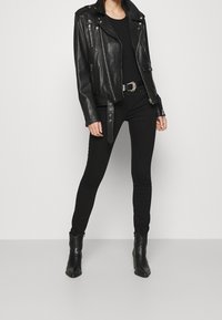 Černá kožená motorkářská bunda se stříbrnými doplňky, těsný černý top a úzké černé džíny. Dokončeno černými kotníkovými botami.