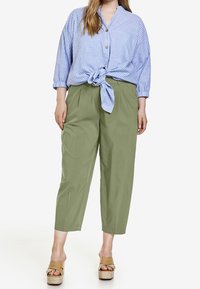 Světlomodrá pruhovaná košile se zapínáním na knoflíky, zavázaná v pase, doplněná olivově zelenými volnými kalhotami a hnědými sandály na platformě.