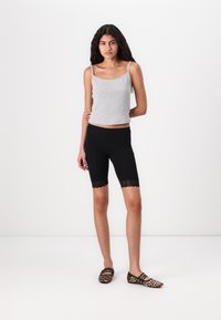 Grå bomulds tanktop med tynde stropper, parret med sorte cykelshorts med blonder, og flade sko med dyreprint. Minimalistisk design.