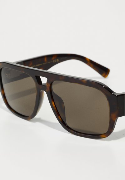 Ochelari de soare din tortoiseshell cu lentile pătrate, nuanță închisă de maro, ramă largă și o tăietură subtilă între lentile pentru un design modern.