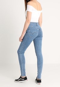 Úzké modré džíny s vysokým pasem, vyrobené z denimové látky. Pár černých bot Vans a bílé top bez ramínek. Jednoduchý design.