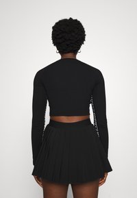 Svart långärmad cropped topp med texturerad tyg och logotypdetaljer på ärmarna, i kombination med en veckad svart mini kjol.