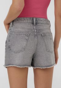 Shorts in denim grigio con orlo sfilacciato, dotati di due tasche posteriori e una vestibilità classica. Il materiale presenta lievi segni di usura. Progettati per un abbigliamento casual.