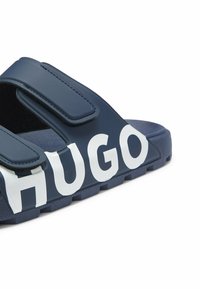 Sandale slide bleu marine avec double bride ajustable et grand logo blanc "HUGO" sur la bride supérieure et le bord de la semelle.