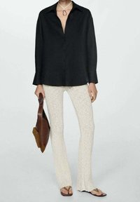 Camicia nera con bottoni, pantaloni leggeri a coste color crema, sandali piatti marroni e borsa a spalla marrone. Tessuto dal tocco liscio e vestibilità rilassata.