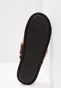 Semelle extérieure noire en caoutchouc d'une pantoufle avec un motif étoile texturé, présentant une tige supérieure douce à imprimé animal visible sur le bord.