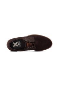 Zapato de ante marrón con una textura suave, punta redonda y detalles en cuero marrón. Presenta una suela plana y un diseño tradicional de cordones.