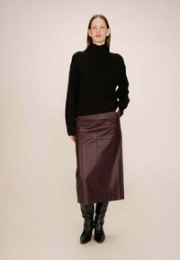 Pull en maille côtelée noir avec un col roulé associé à une jupe en cuir bordeaux ajustée. Complète avec des bottes noires à talons hauts. Design simple et épuré.