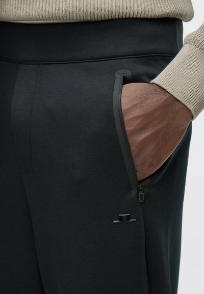 Μαύρο αθλητικό παντελόνι με τσέπη με φερμουάρ, με λεία υφή και διακριτική λεπτομέρεια λογότυπου. Η μέση έχει ριμπ ύφασμα και είναι εφαρμοστή.