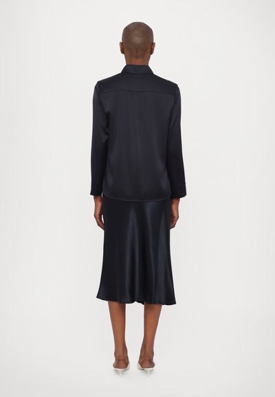 Black satin shirt dress with long sleeves and a flowing silhouette, featuring a back yoke and knee-length hem. Smooth texture with subtle sheen.