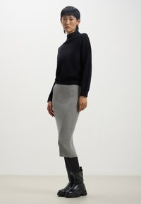 Maglione a collo alto nero abbinato a una gonna midi grigia a coste. La modella indossa stivali neri a punta larga, mostrando una silhouette aderente.
