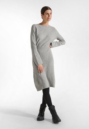 Graues Strickkleid mit langen Ärmeln, rundem Ausschnitt und seitlichen Schlitzen, kombiniert mit schwarzen kniehohen Stiefeln und schwarzen Leggings.